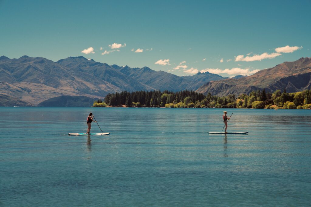 Two people stand-up paddleboarding on a calm mountain lake